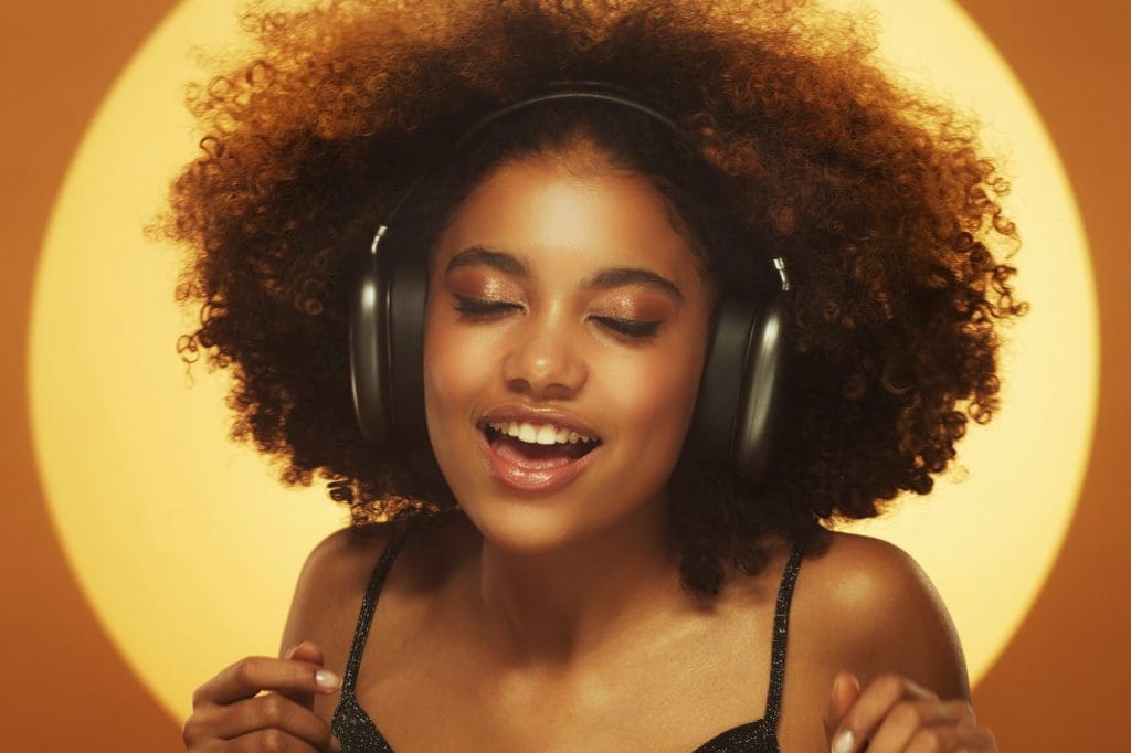 African woman singing a song, wearing headphones, isolated on brown studio background