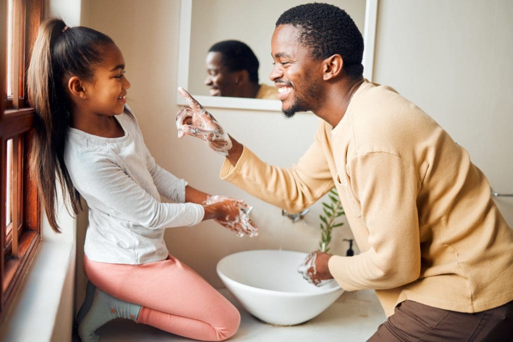 Black family, washing hands and health care with soap to clean in home bathroom. Man teaching girl