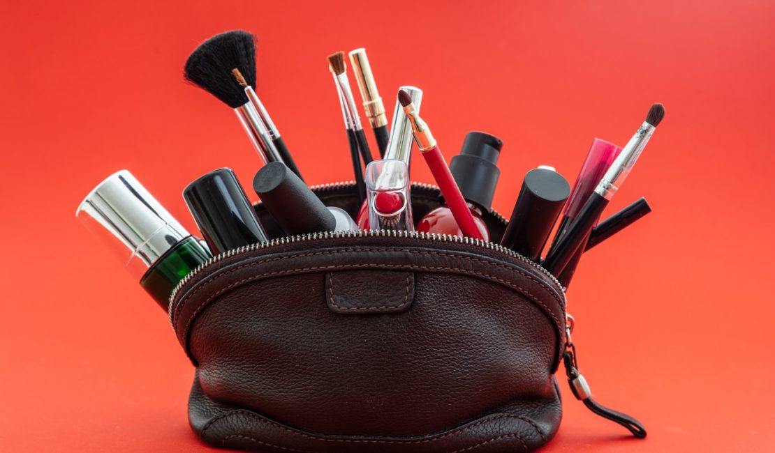 Make-up bag with cosmetics and makeup accessories against red background