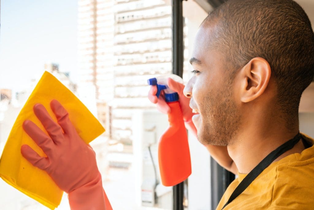 Male housekeeper cleaning glass window at home.