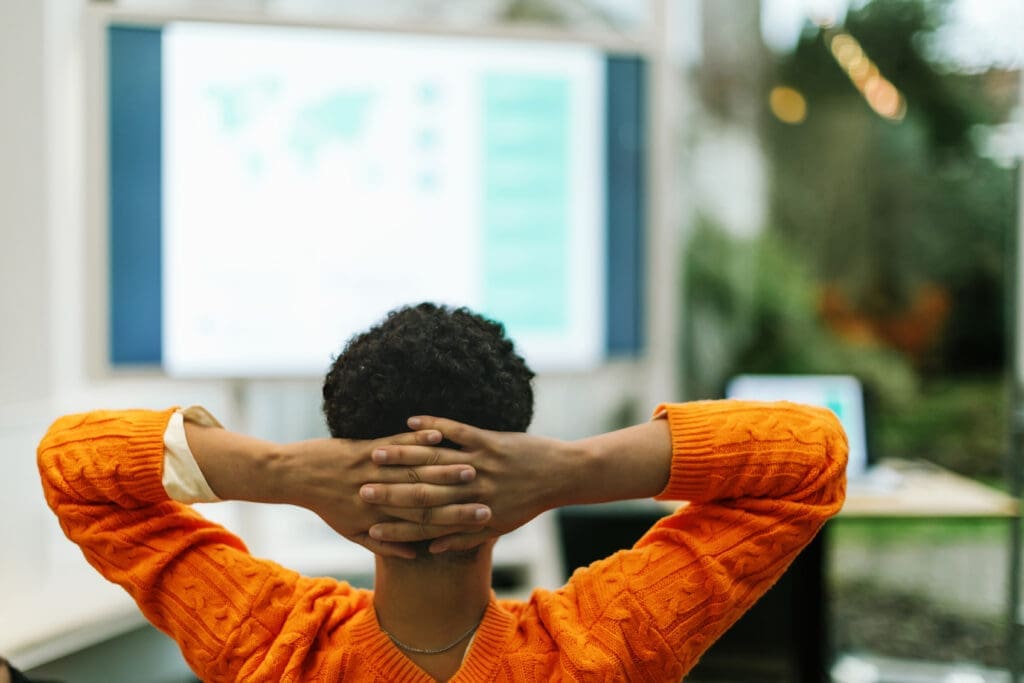 view from behind of a woman at work with her hands clasped behind her head