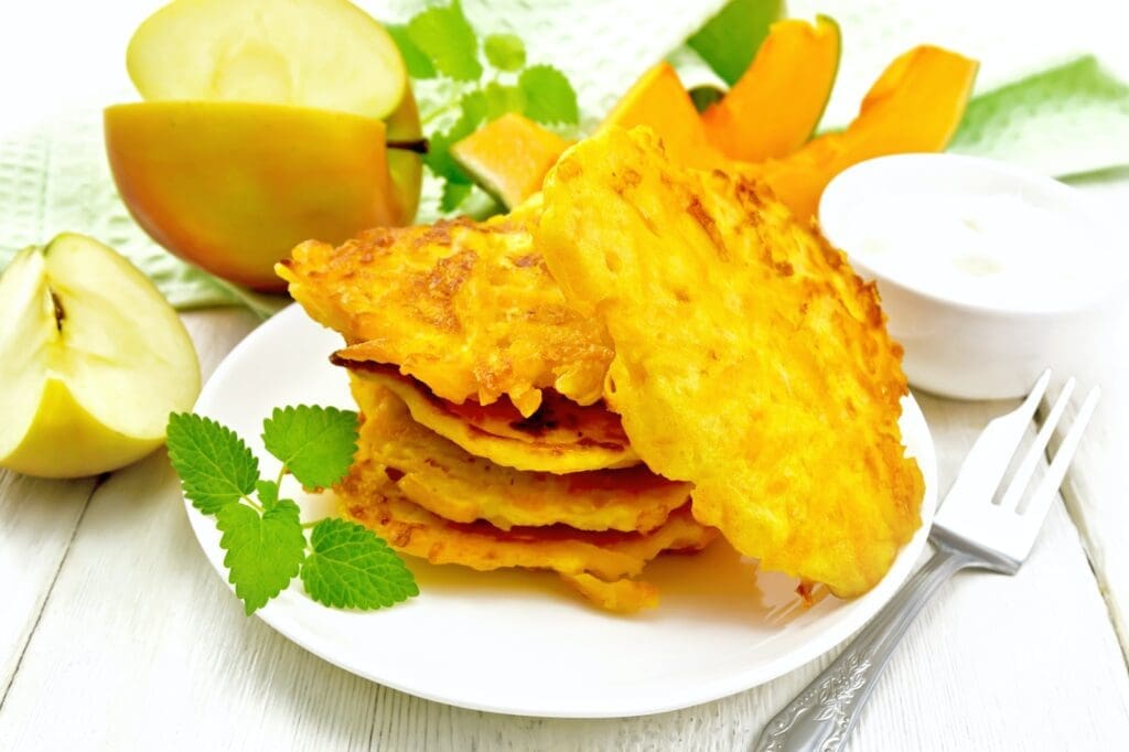 Pancakes of pumpkin with apple in plate on white board