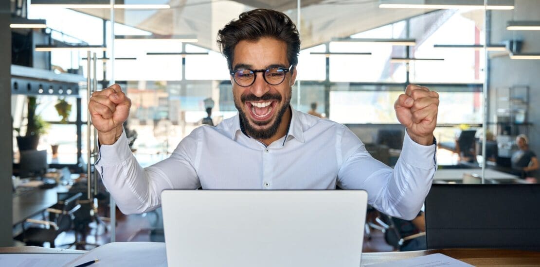 Excited business man celebrating success looking at laptop in office.