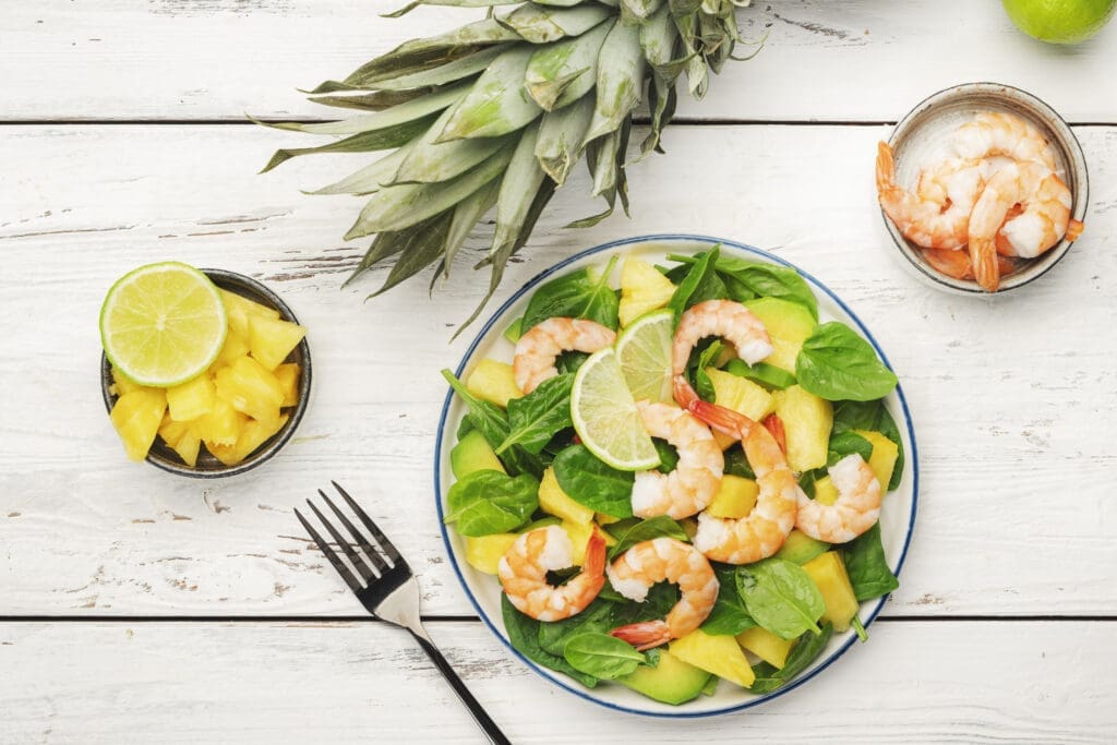 Pineapple shrimp salad with spinach, avocado and lime on white wooden kitchen table, top view